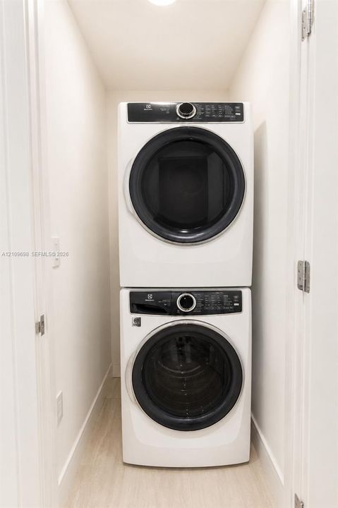 Laundry closet featuring a white, stackable front-loading washer and dryer set