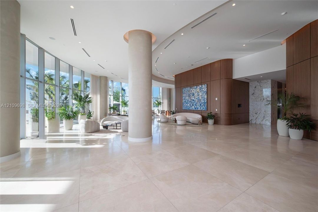 Expansive interior space featuring floor-to-ceiling windows, polished stone flooring, curved architectural pillars, wood-panelled accent walls, and recessed ceiling lighting