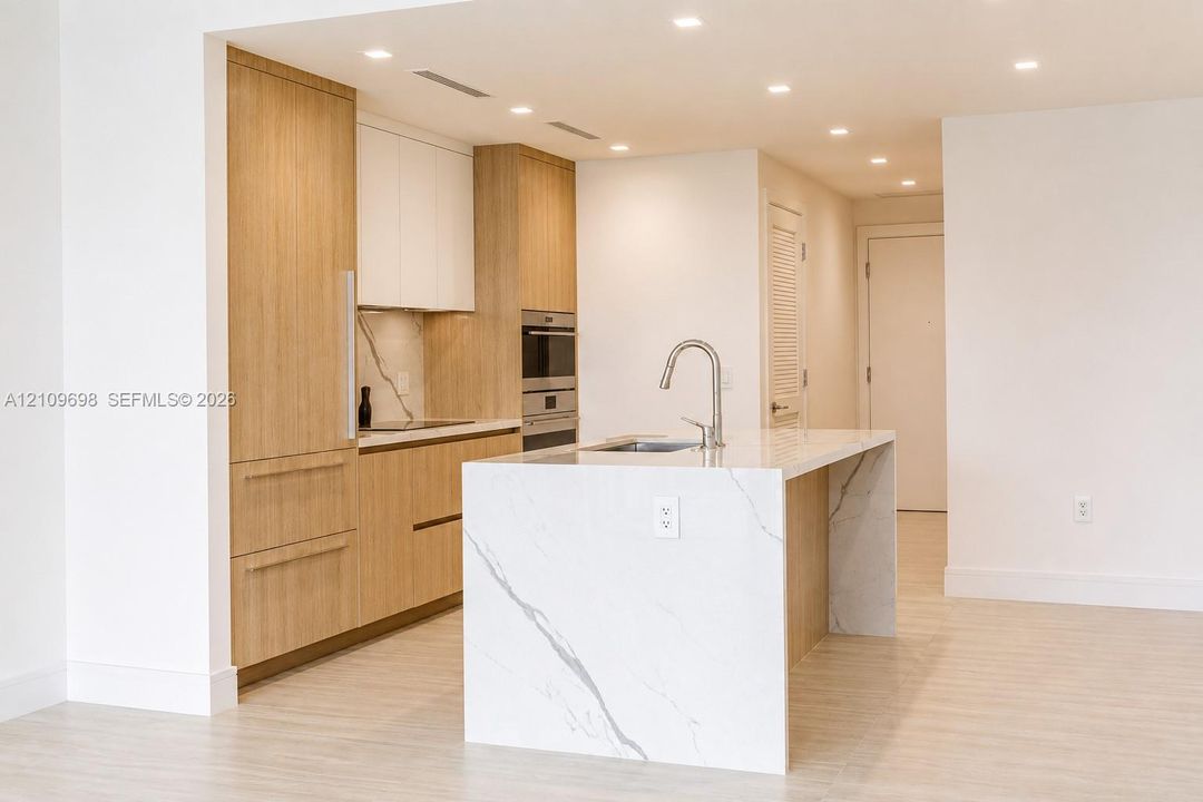 Kitchen featuring wood-finish cabinetry, stone-style waterfall island, recessed lighting, integrated appliances, and stone-style backsplash