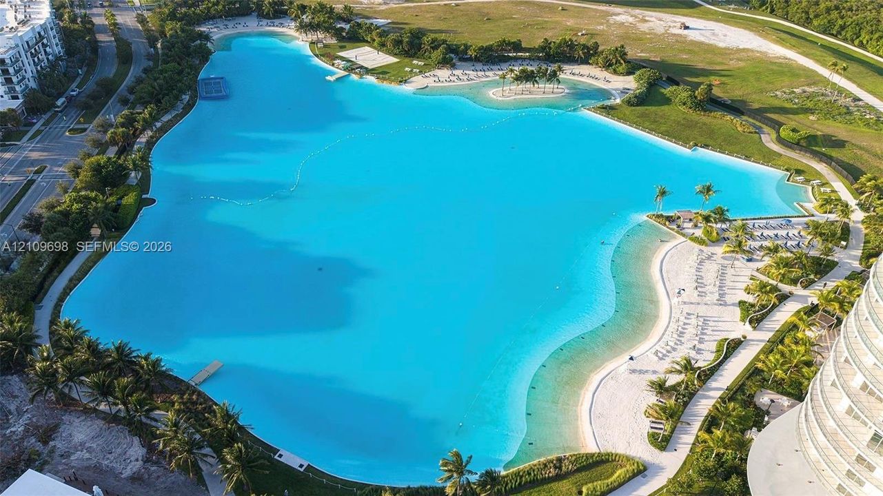 Expansive turquoise lagoon featuring sandy shorelines, walking paths, landscaped palm trees, and an island formation