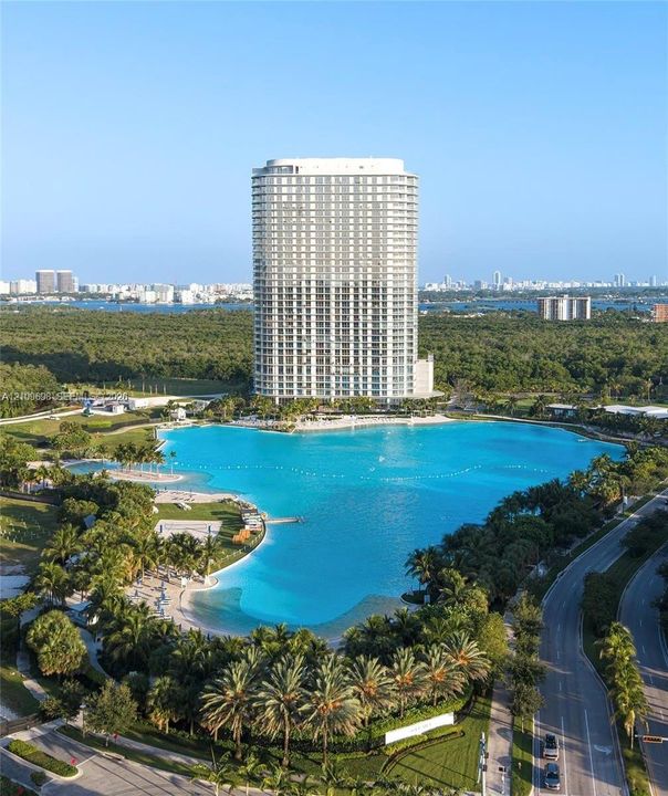 High-rise residential tower featuring floor-to-ceiling windows, expansive man-made lagoon, white sand beaches, and lush tropical landscaping