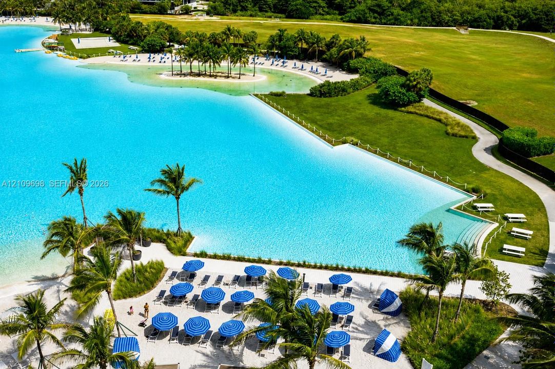 Man-made lagoon featuring a white sand beach, extensive perimeter landscaping, walking paths, and concrete terraced stairs leading to the water