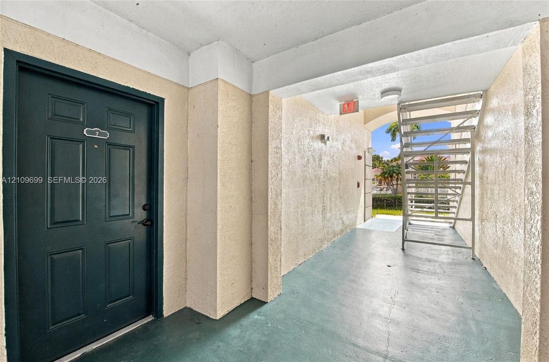 Covered entryway featuring a solid-panel door, textured stucco exterior walls, and concrete flooring