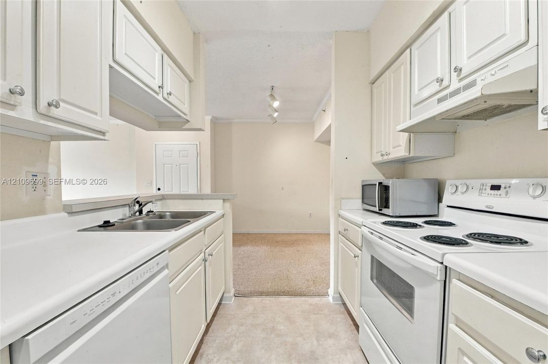 Kitchen featuring white shaker-style cabinetry, solid-surface countertops, dual-basin stainless steel sink, and white appliances
