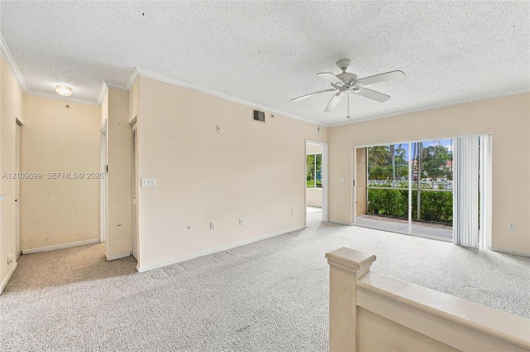 Neutral-toned living space featuring wall-to-wall carpeting, a ceiling-mounted fan with light fixture, and large sliding glass doors providing outdoor access