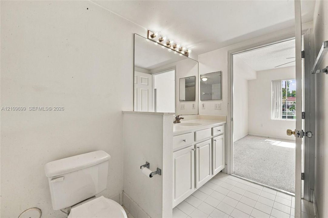Bathroom featuring white cabinetry, an integrated basin, a wall-mounted light fixture, a large mirror, and tiled flooring