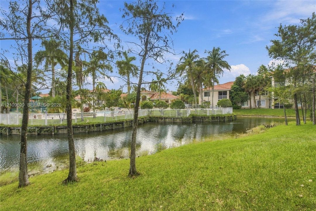 Waterfront property featuring a manicured lawn, mature palm trees, and a perimeter security fence