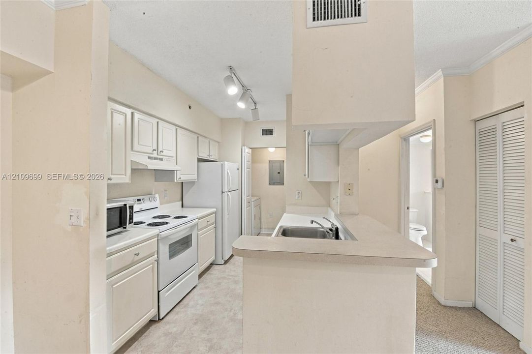 Kitchen featuring white cabinetry, solid-surface countertops, track lighting, a stainless steel dual-basin sink, and louvered bi-fold closet doors