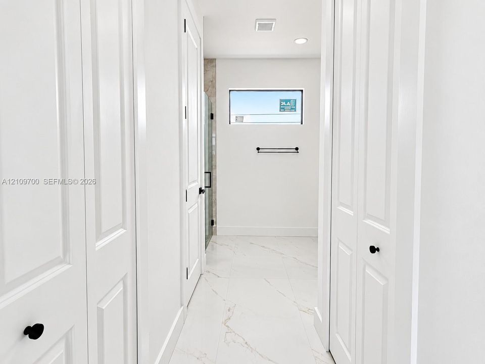 Hallway featuring white paneled doors with matte black hardware, large-format tile flooring with marble-style veining, recessed lighting, and a horizontal window