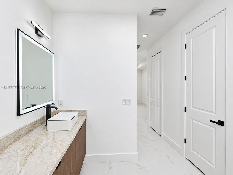 Vanity featuring stone-finish countertop, wood-finish cabinetry, rectangular vessel sink, matte black faucet, and an integrated LED-lighted mirror