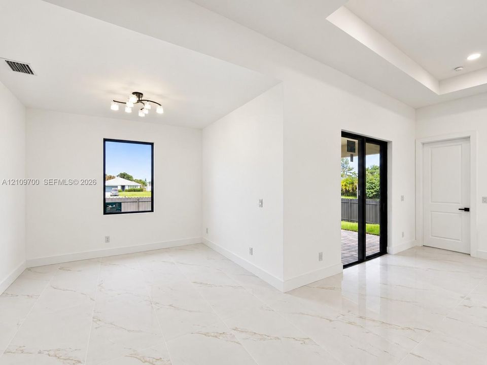 Interior space featuring large-format veined tile flooring, tray ceilings, multi-light modern ceiling fixture, black-framed windows, and sliding glass doors
