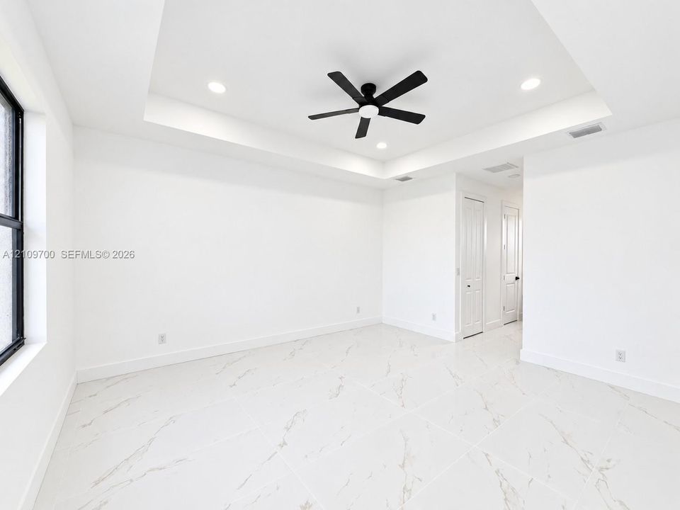 Tray ceiling featuring a central matte black ceiling fan, recessed lighting, and large-format tile flooring with marble-style veining