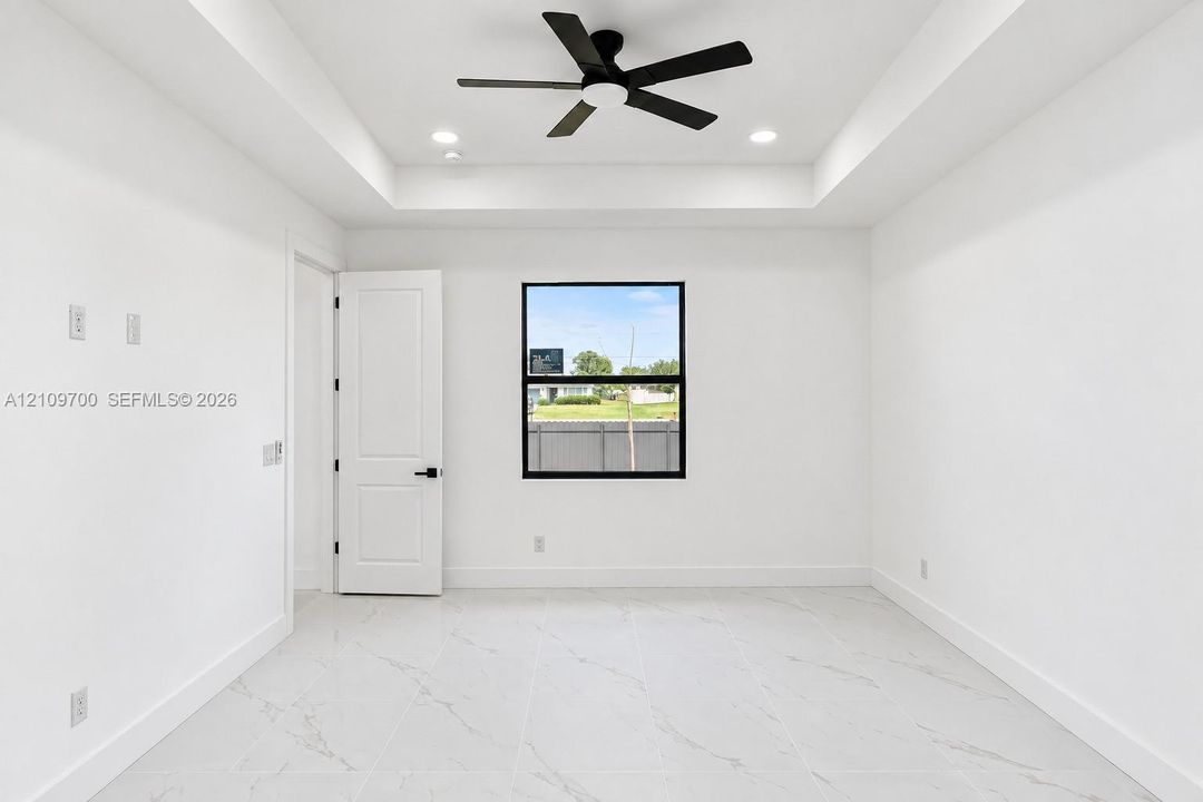 Interior space featuring a recessed tray ceiling, large-format tile flooring with marble-finish veining, a matte black ceiling fan, and black-framed window casing