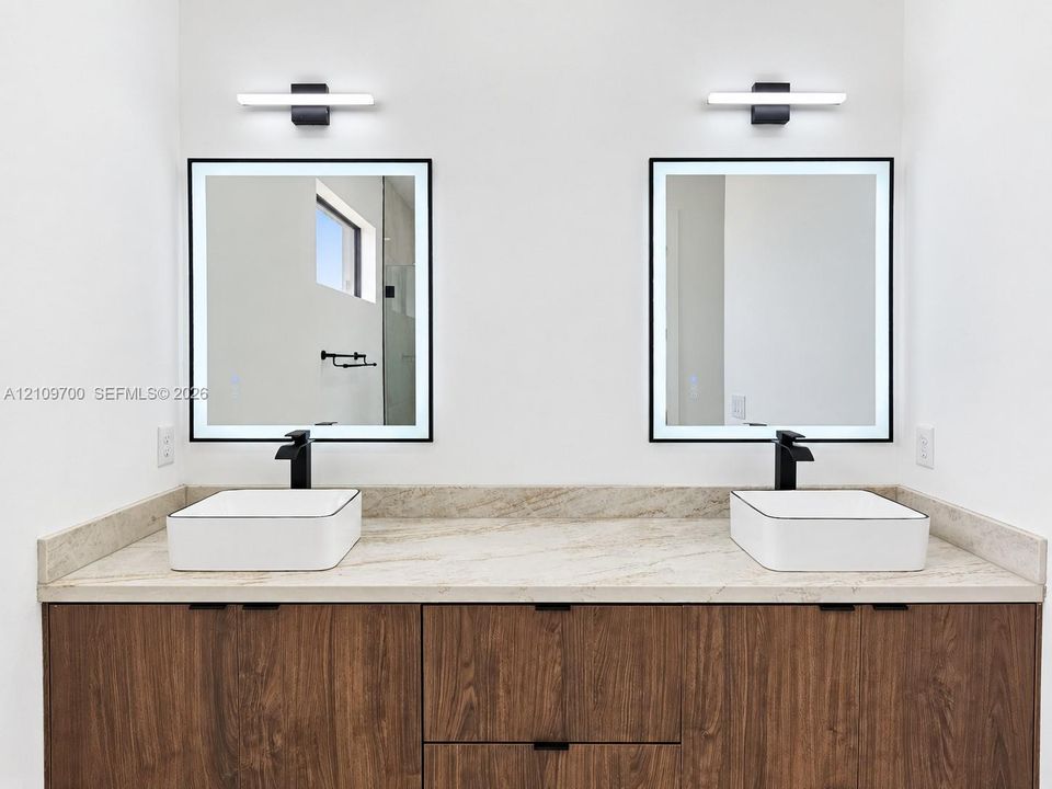 Dual vanity featuring a stone countertop, square vessel sinks, matte black widespread faucets, and integrated LED-backlit mirrors with linear wall-mounted lighting