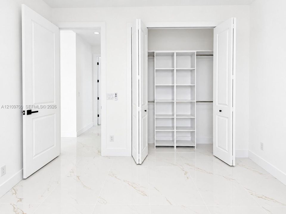 Polished stone-finish tile flooring, walk-in closet with built-in white shelving, and solid-core interior doors with matte black hardware