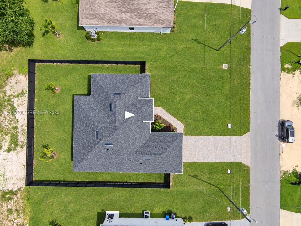 Aerial view of property featuring a fenced backyard, multi-facet shingled roof, paver driveway, and open lot space