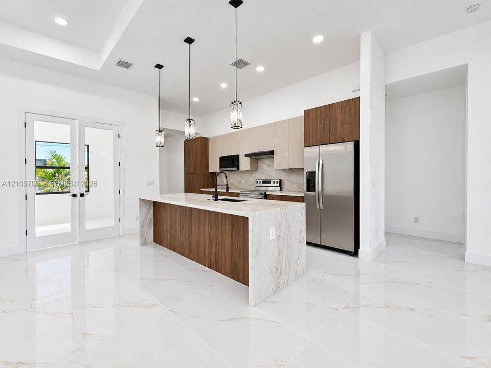 Kitchen featuring a waterfall island with a stone-finish countertop, two-tone cabinetry, stainless steel appliances, pendant lighting, and polished stone-finish flooring