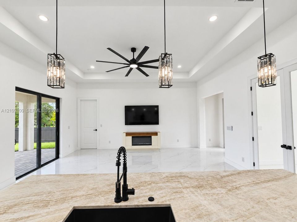 Tray ceiling with recessed lighting and a multi-blade ceiling fan, expansive stone-finish flooring, and natural stone kitchen island countertop featuring a matte black industrial faucet and undermount sink