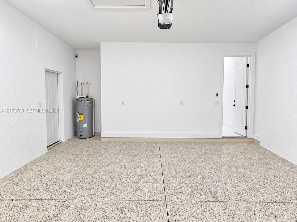 Garage interior featuring finished epoxy flooring, white painted walls, two access doors, and an integrated water heater