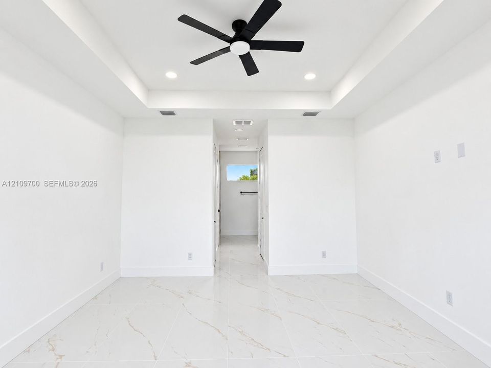 Tray ceiling featuring a matte black multi-blade ceiling fan, recessed lighting, and large-format tile flooring with veining