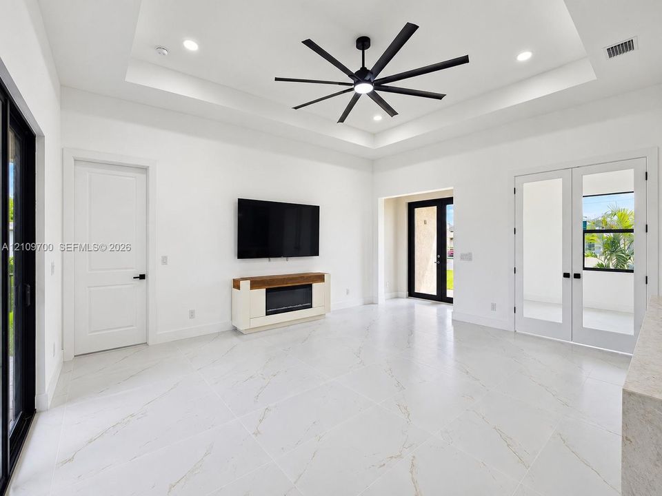 Tray ceiling with recessed lighting, large-format tile flooring, multi-blade ceiling fan, built-in electric fireplace, and French doors