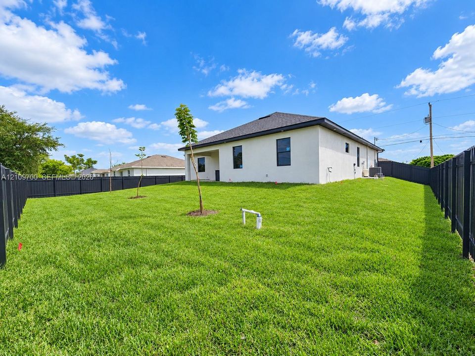 Expansive backyard featuring a manicured lawn, dark-toned perimeter fencing, and exterior stucco siding