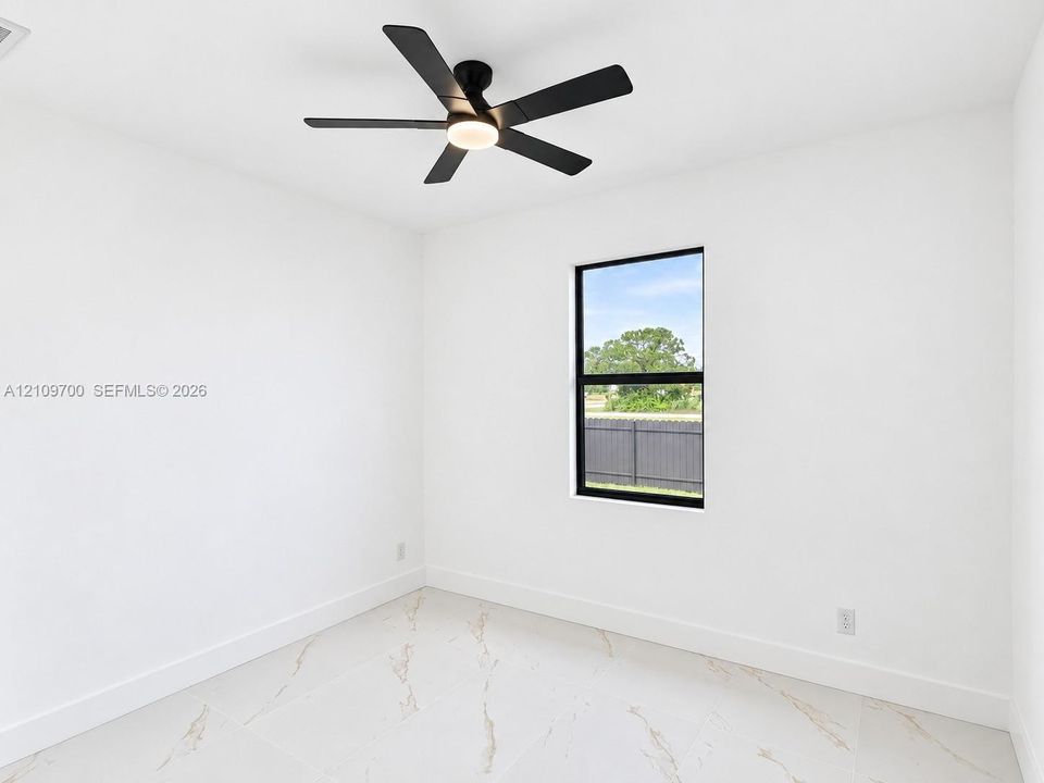 Interior space featuring large-format tile flooring with marble-style veining, a matte black ceiling fan with integrated lighting, and a window with a matte black frame