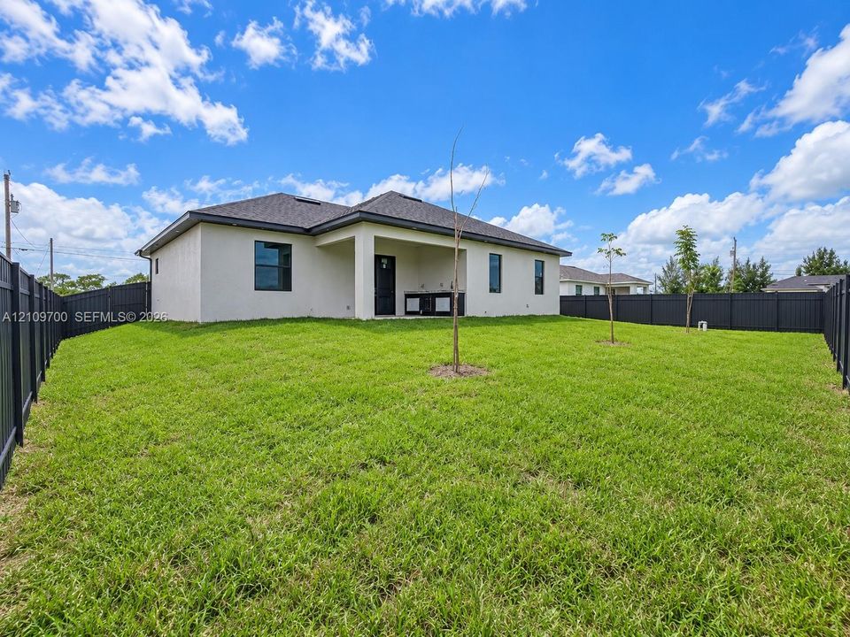 Spacious backyard featuring a perimeter privacy fence, covered rear patio, and outdoor kitchen cabinetry
