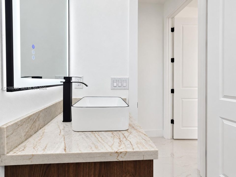 Stone countertop vanity featuring a rectangular vessel sink, matte black tall-spout faucet, and a wall-mounted LED-backlit mirror