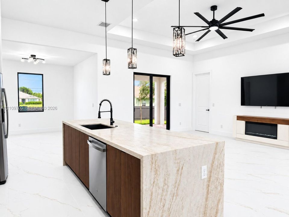 Large kitchen island with a stone-finish countertop, dual-tone cabinetry, recessed ceiling with a multi-blade fan, custom pendant lighting, and an integrated electric fireplace