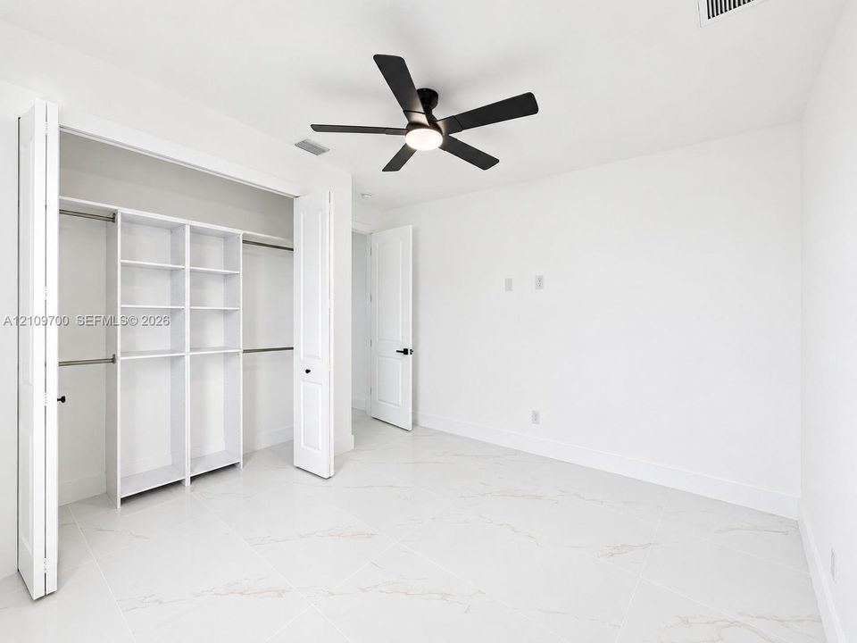 Interior space featuring large-format tile flooring with marble-pattern veining, a ceiling fan with integrated lighting, and a closet system with built-in shelving and dual hanging rods