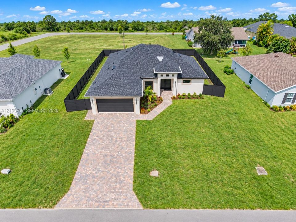 Single-story residence featuring a dark shingle roof, a paved paver driveway, and an enclosed backyard with black metal fencing