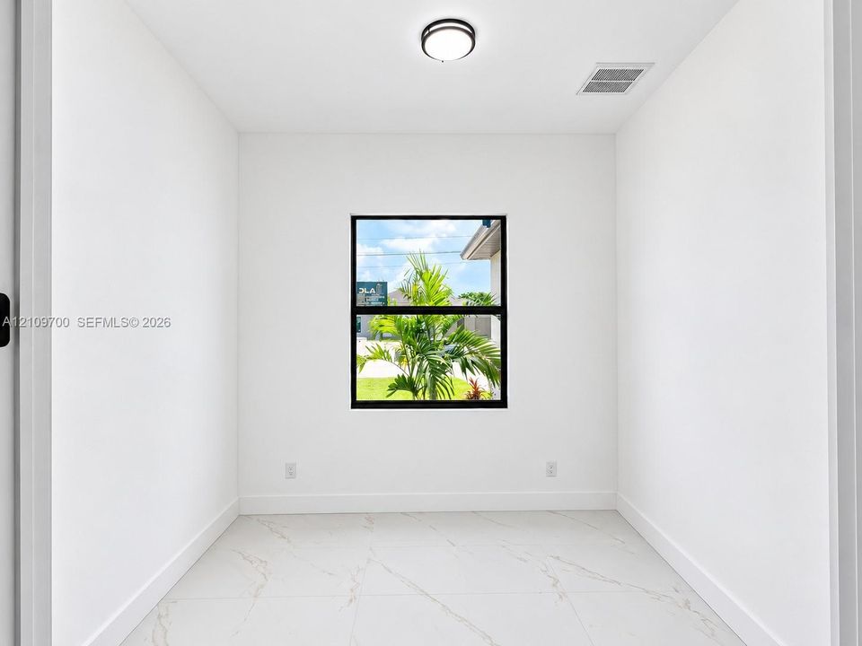 Neutral interior room featuring white walls, large-format tile flooring with veining, and a window with a black frame
