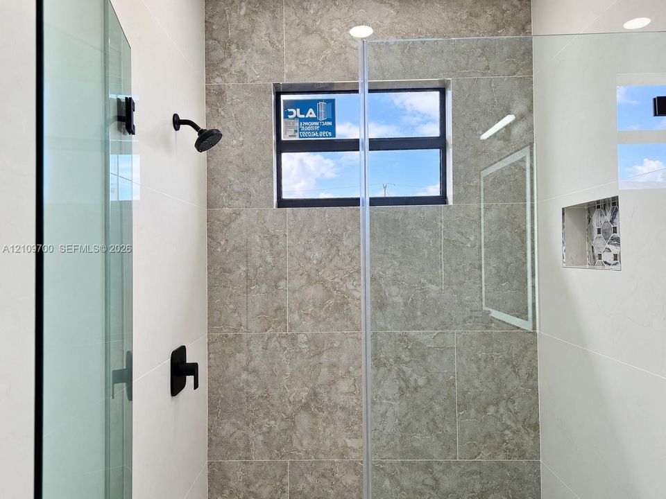 Walk-in shower featuring large-format neutral-toned tile, a frameless glass enclosure, matte black fixtures, a recessed niche, and a horizontal window