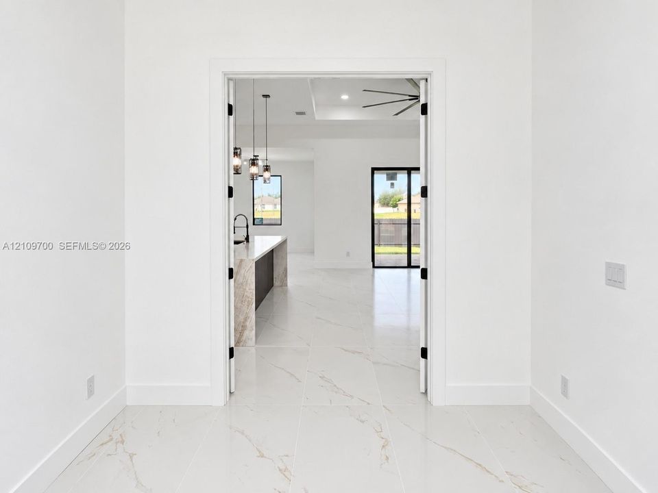 Large-format white tile flooring with veining detail, double-swing interior doors, recessed ceiling lighting, multi-pendant island lighting, and a kitchen island with stone-finish waterfall countertop