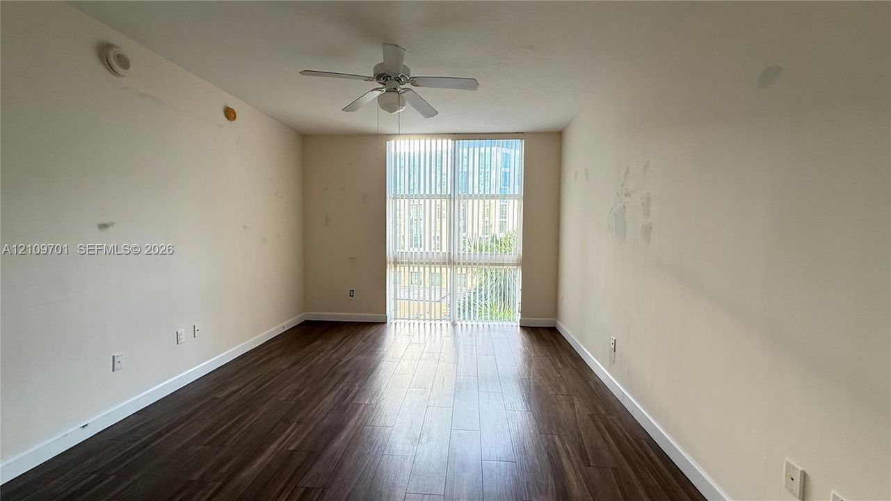 Room featuring wood-finish flooring, a ceiling fan with integrated lighting, and a floor-to-ceiling window assembly with vertical blinds