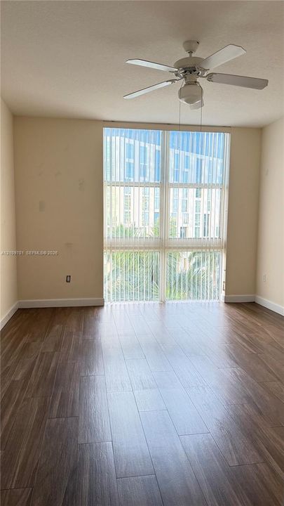 Floor-to-ceiling windows with vertical blinds, wood-finish flooring, and a central ceiling fan