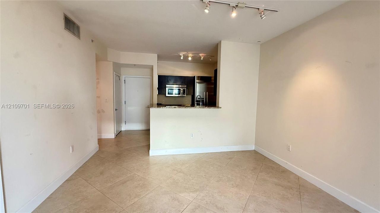 Open-concept area featuring diagonal-set tile flooring, multi-directional track lighting, and a kitchen pass-through counter with stone-surface countertops