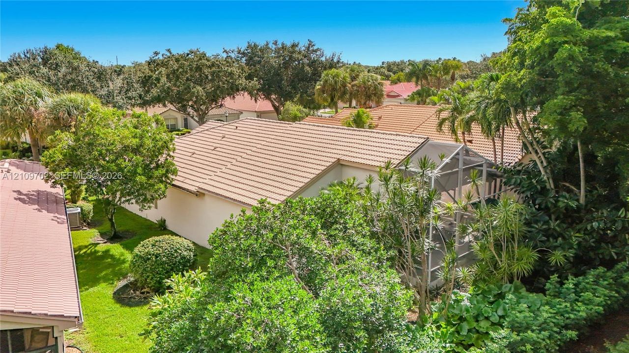 Tile roof architecture featuring a screened-in lanai, mature landscaping, and an expansive lawn