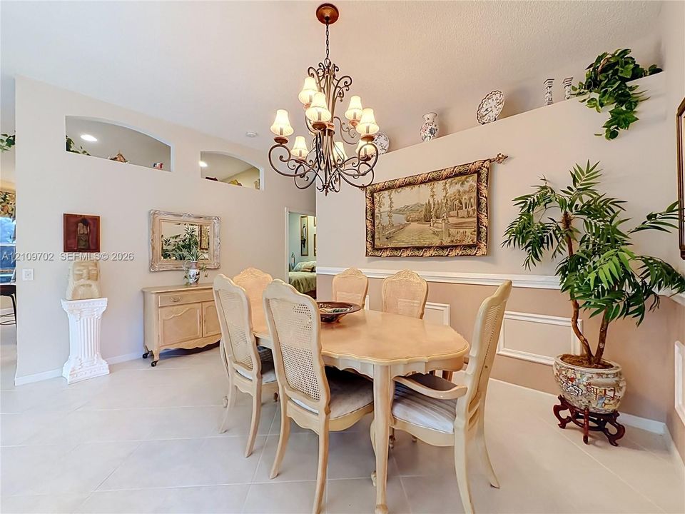 Dining area featuring high ceilings, arched wall niches, decorative chair rail molding, and a wrought iron chandelier