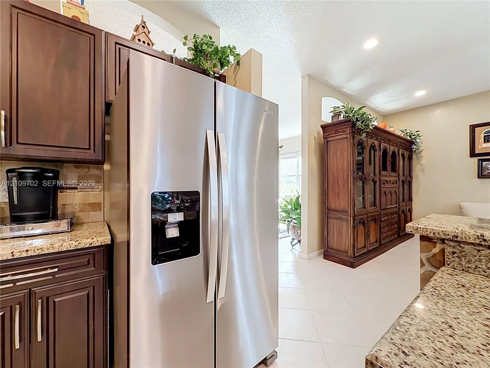 Kitchen featuring dark wood cabinetry, stainless steel side-by-side refrigerator, stone-style countertops, tile backsplash, and recessed lighting