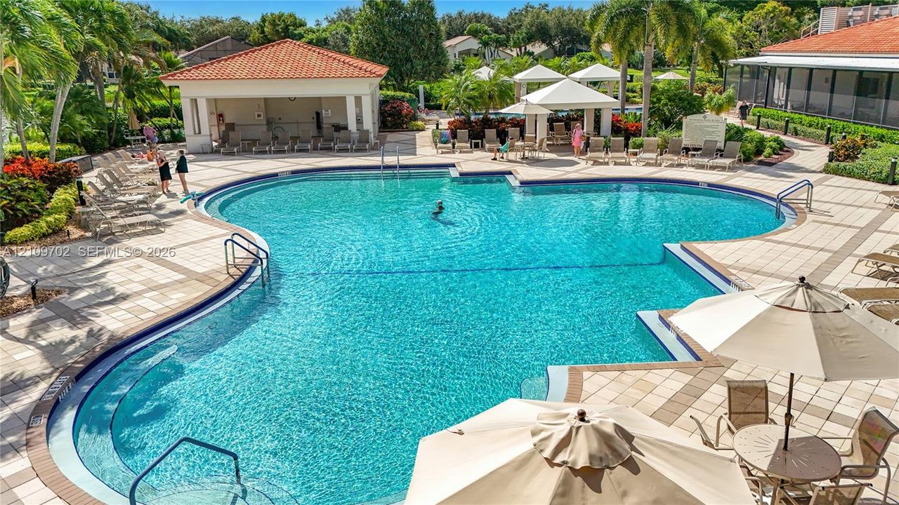 Community swimming pool featuring a geometric design, expansive paved pool deck, and shaded pavilion structures with terracotta-style roof tiles