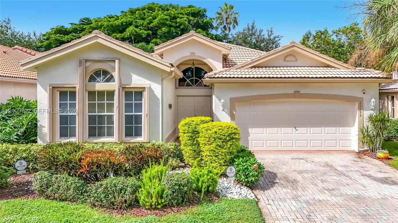 Stucco exterior featuring arched windows, tile roof, and a paved stone driveway