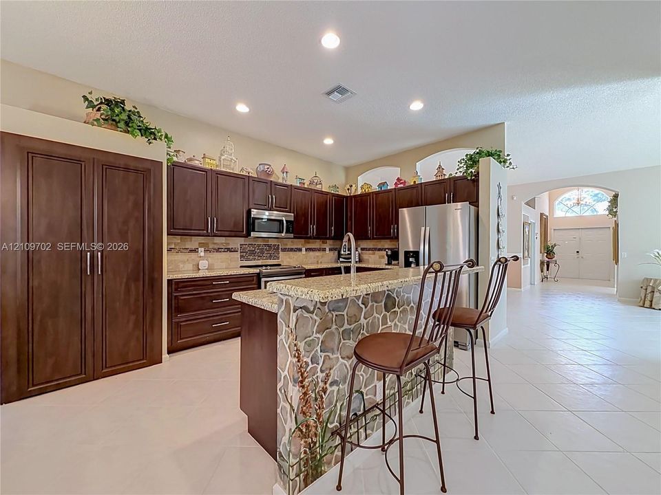 Kitchen featuring dark wood cabinetry, stone-veneer breakfast bar base, stone-tile backsplash, and recessed lighting