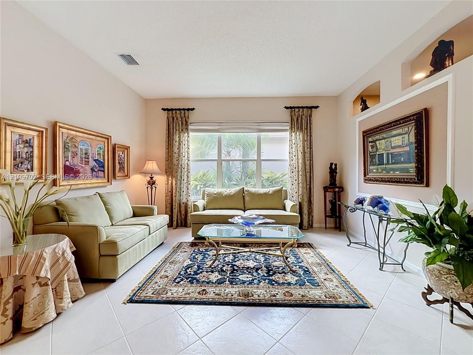Living area featuring high ceilings, neutral tile flooring, recessed wall niches, and large windows with exterior greenery