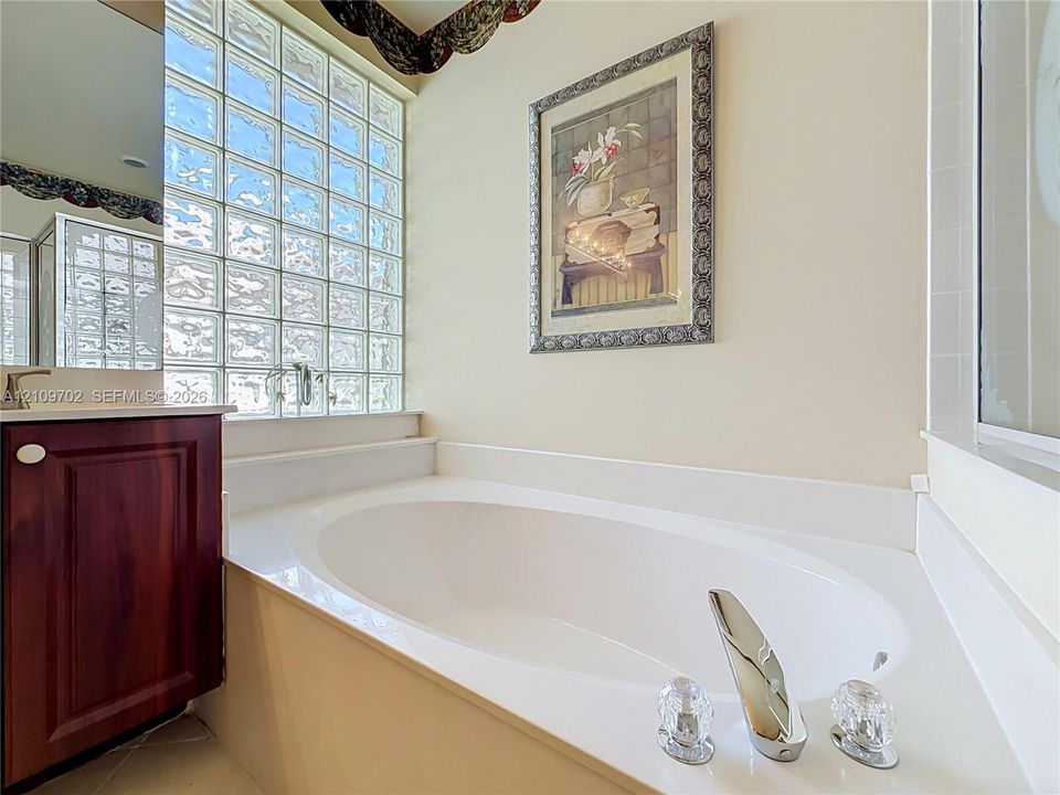 Soaking tub with chrome faucet fixtures, glass block window, and dark wood-finish cabinetry