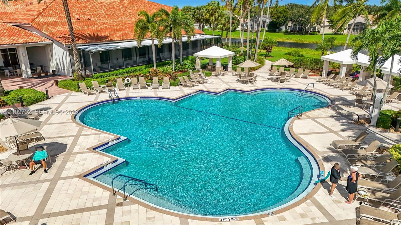 Large, irregular-shaped swimming pool with tile surround, multiple covered cabanas, and manicured landscaping