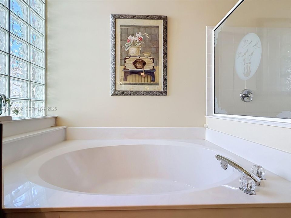 Oval soaking tub featuring a wide surround, glass block window, and deck-mounted polished chrome faucet with crystal-style handles