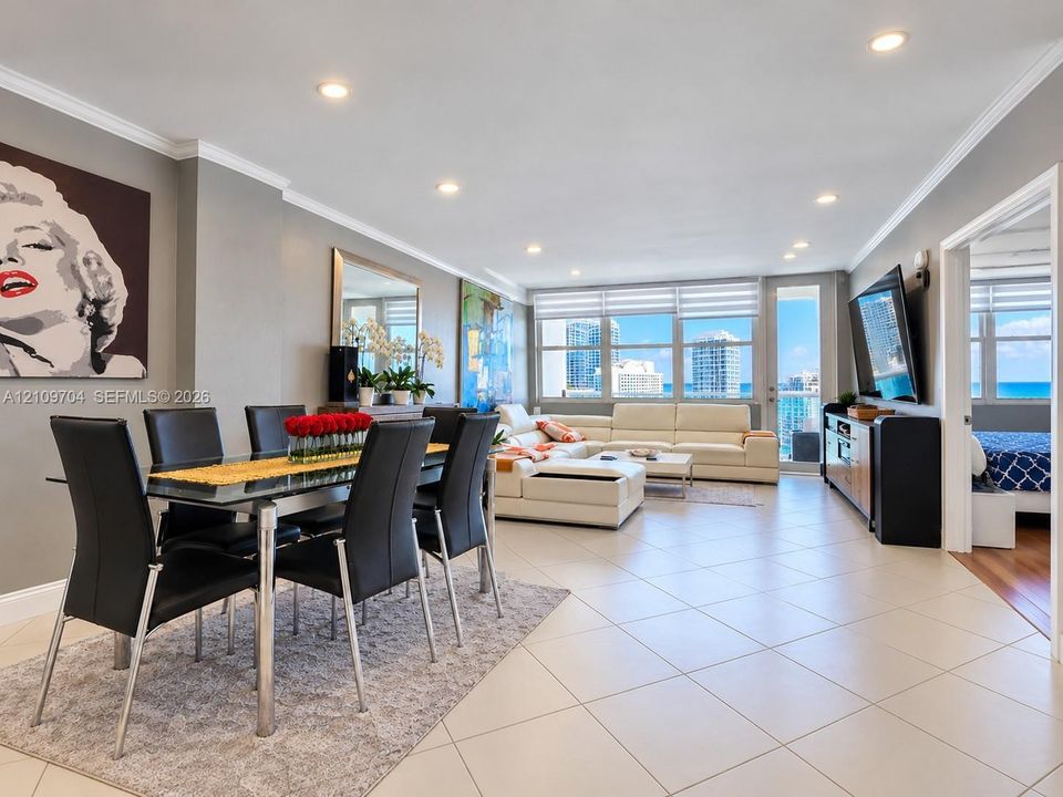 Open-concept floor plan featuring large-format ceramic tile flooring, recessed lighting, crown molding, and floor-to-ceiling windows with balcony access