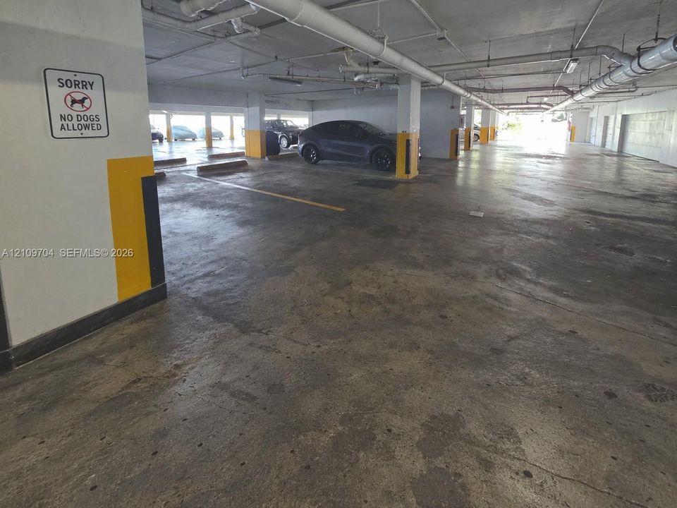 Covered parking area featuring concrete flooring, structural support columns, and overhead utility systems